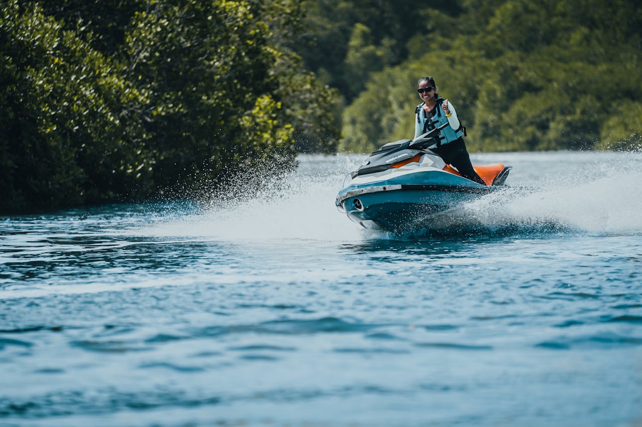 Woman enjoying a thrilling jet ski ride on a vibrant lake surrounded by lush greenery.